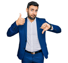 Wall Mural - Young hispanic man wearing business jacket doing thumbs up and down, disagreement and agreement expression. crazy conflict