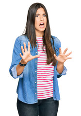 Wall Mural - Young brunette woman wearing casual clothes afraid and terrified with fear expression stop gesture with hands, shouting in shock. panic concept.