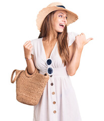 Wall Mural - Young beautiful blonde woman wearing summer dress and wicker handbag pointing thumb up to the side smiling happy with open mouth