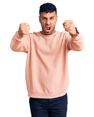 Canvas Print - Young hispanic man wearing casual clothes angry and mad raising fists frustrated and furious while shouting with anger. rage and aggressive concept.