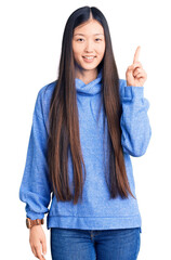 Wall Mural - Young beautiful chinese woman wearing casual turtleneck sweater showing and pointing up with finger number one while smiling confident and happy.