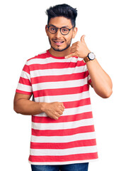 Poster - Handsome latin american young man wearing casual clothes and glasses smiling doing phone gesture with hand and fingers like talking on the telephone. communicating concepts.