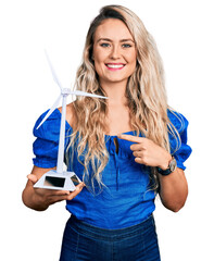 Canvas Print - Young blonde woman holding solar windmill for renewable electricity smiling happy pointing with hand and finger