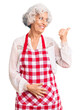 © Krakenimages.com - Senior grey-haired woman wearing apron smiling with happy face looking and pointing to the side with thumb up.