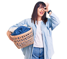 Poster - Young plus size woman holding laundry basket smiling happy doing ok sign with hand on eye looking through fingers