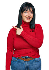 Poster - Young hispanic woman wearing casual clothes cheerful with a smile of face pointing with hand and finger up to the side with happy and natural expression on face