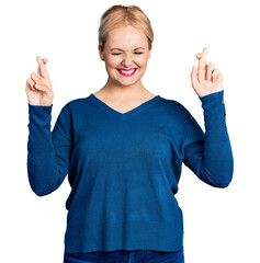 Wall Mural - Young blonde woman wearing casual clothes gesturing finger crossed smiling with hope and eyes closed. luck and superstitious concept.