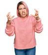© Krakenimages.com - Hispanic woman with pink hair wearing casual winter sweater shouting frustrated with rage, hands trying to strangle, yelling mad