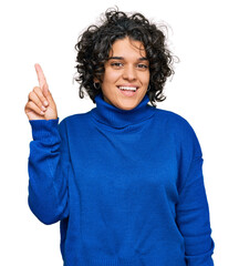 Canvas Print - Young hispanic woman with curly hair wearing turtleneck sweater pointing finger up with successful idea. exited and happy. number one.