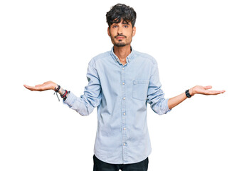 Poster - Young hispanic man wearing casual clothes clueless and confused expression with arms and hands raised. doubt concept.