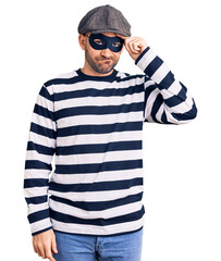 Wall Mural - Young handsome man wearing burglar mask worried and stressed about a problem with hand on forehead, nervous and anxious for crisis