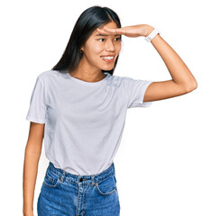 Sticker - Beautiful young asian woman wearing casual white t shirt very happy and smiling looking far away with hand over head. searching concept.