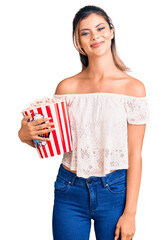 Canvas Print - Young beautiful woman holding popcorn looking positive and happy standing and smiling with a confident smile showing teeth