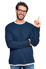 Sticker - Young hispanic man wearing casual clothes and glasses with a big smile on face, pointing with hand and finger to the side looking at the camera.