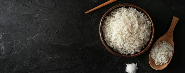 Wall Mural - Bowl of white rice with wooden spoon and salt on dark background