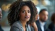 © G.Go - A woman with curly hair is sitting in a room with other people