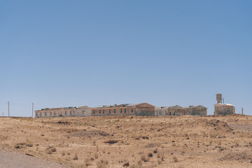 a desolate desert landscape with a few buildings in the distance. the sky is clear and blue, and the