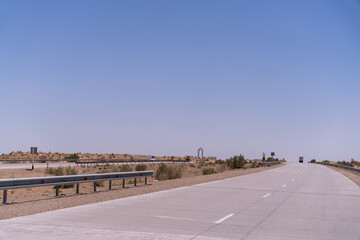 Wall Mural - A long, empty road with a blue sign in the distance. The sky is clear and blue