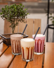 Wall Mural - Three milkshakes with chocolate sauce standing on wooden table