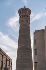 Wall Mural - A tall brick tower with a pointed top stands in front of a building. The sky is clear and blue, with a few clouds scattered in the background