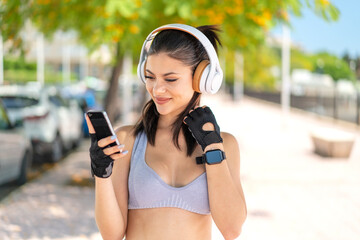 Wall Mural - Young pretty sport woman at outdoors listening music and looking to mobile