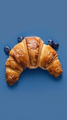 Poster - A croissant with blueberries on top of it. The blueberries are scattered around the croissant, and the croissant is sitting on a blue background