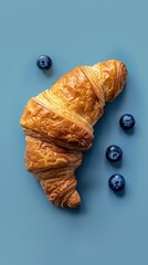 Poster - A croissant with blueberries on top of a blue background. The croissant is the main focus of the image, but the blueberries add a pop of color and contrast to the scene