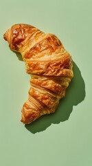 Poster - A croissant is shown on a green background. The croissant is golden brown and has a slightly crispy texture. Concept of indulgence and comfort