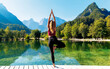 © M.studio - beautiful attractive woman practice yoga, standing on wooden pier looking at green lake and mountain