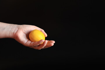 Close-up of a woman's hand holding a ripe lemon. Yellow lemon in hand on a black background. Ingredient. Fruit and food concept. Citrus