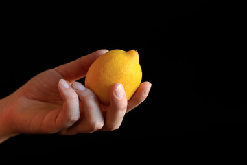 Close-up of a woman's hand holding a ripe lemon. Yellow lemon in hand on a black background. Ingredient. Fruit and food concept. Citrus