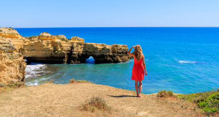 Wall Mural - woman tourist wearing red dress enjoying panorama view of algarve beach and coast landscape- portuga