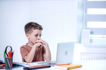 School kid with computer having video conference chat with teacher and class group. Child studying from home. Homeschooling. Modern gadgets for education. Screen time control. Online remote learning.