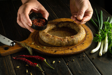 Wall Mural - Man hands adding aromatic spices to meat sausage on cutting board. Concept of cooking delicious lunch with meat sausage at home.