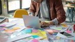 © Jojo - A designer working on a laptop with sketches and prototypes spread out