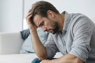 Wall Mural - A stressed man is sitting on a couch with his head in his hands. He looks sad and is frowning
