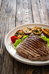 Wall Mural - Grilled beef steak with baked potatoes and fresh vegetables on wooden table