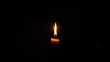 © Karolis - A single candle with a bright flame stands alone in the darkness, casting a warm light.