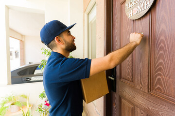 Cheerful delivery man with a package is at the front door of a house, ready to deliver a parcel