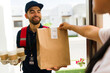 © AntonioDiaz - Cheerful delivery person is handing over a paper bag and a cardboard tray of coffee cups to a customer at their front door