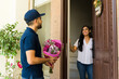 © AntonioDiaz - Latin delivery man with a cheerful smile delivering a bouquet of flowers to a young woman at her doorstep
