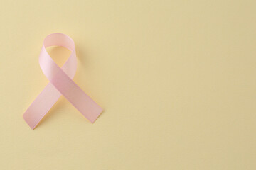 Wall Mural - Pink awareness ribbon on pale yellow background, top view