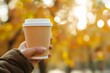 © zakiroff - Coffee cup in hand with autumn leaves in background, mockup, copy space concept