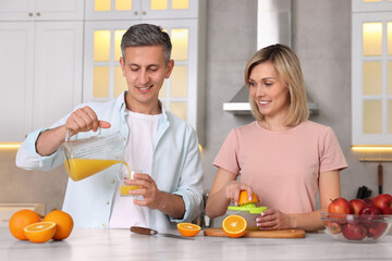 Poster - Happy couple with juicer and fresh products making juice at white marble table in kitchen