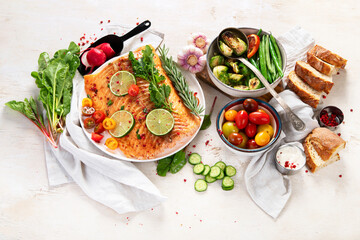 Wall Mural - Grilled salmon and vegetables on wooden light background. Dinner table with cooked fish, tomatoes, asparagus