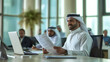 © J - Young Arab men from the Middle East are in the conference room, smiling at a video conference on a laptop, the office processing papers, bills and agreements in hand
