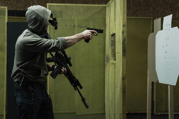 Tactical rifle and pistol shooting at an indoor shooting range. A man in a hood with a night vision device is training to shoot at a target.