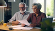 © NOPPHINAN - Senior couple sitting at a dining table, reviewing their retirement plans with financial documents spread out calculator and a laptop.