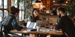 © kwanchaift - A team of three young entrepreneurs discussing strategy around a table with laptops and coffee cups, showing the dynamic energy of a small business
