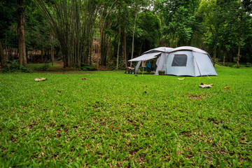 camping white cabin tent on grass campground and tree in nature green forest and autumn camp in garden jungle to holiday relax or vacation travel trip with family trekking on lawn at pha tad waterfall